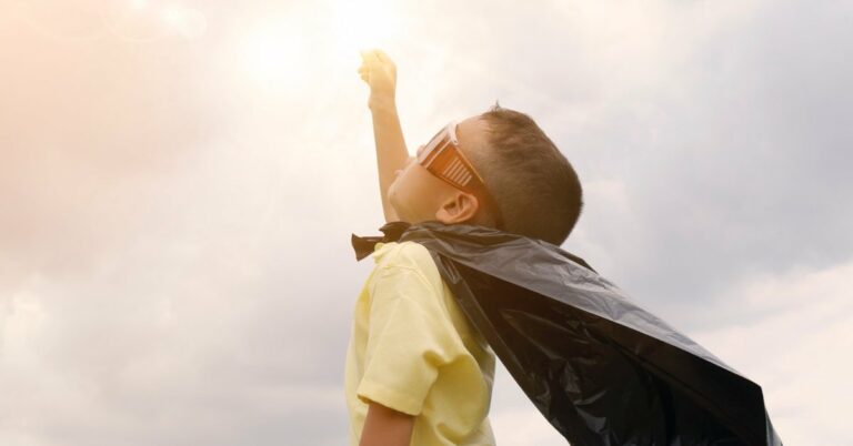 Child with cape and sunglasses reaching for the sky