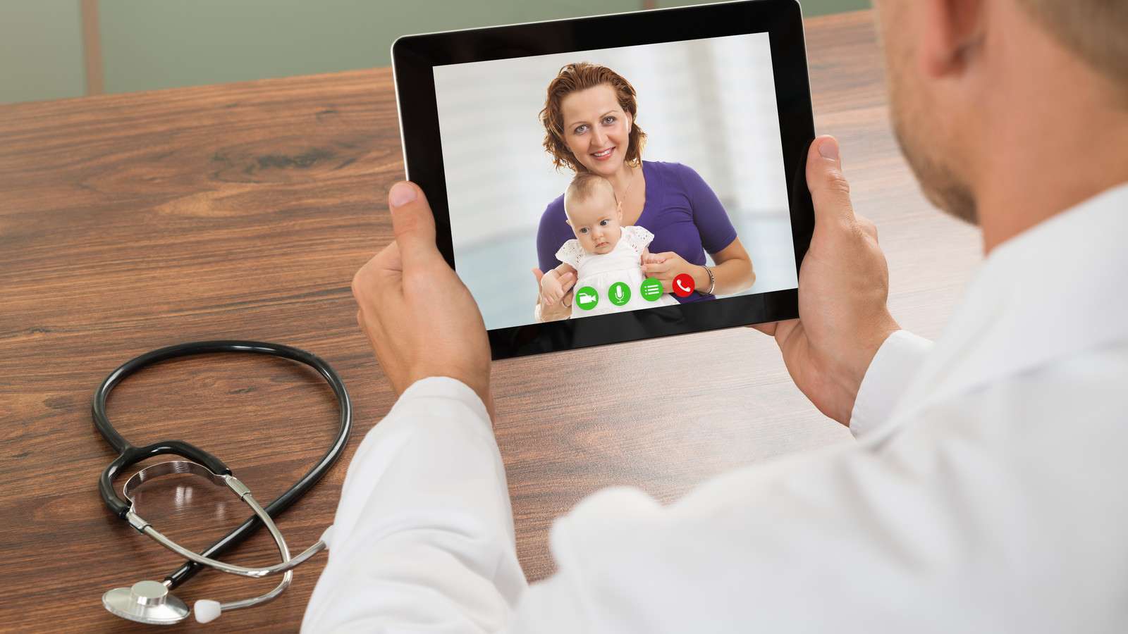 doctor during a telehealth visit with a mom and her baby via an ipad. stethoscope on table