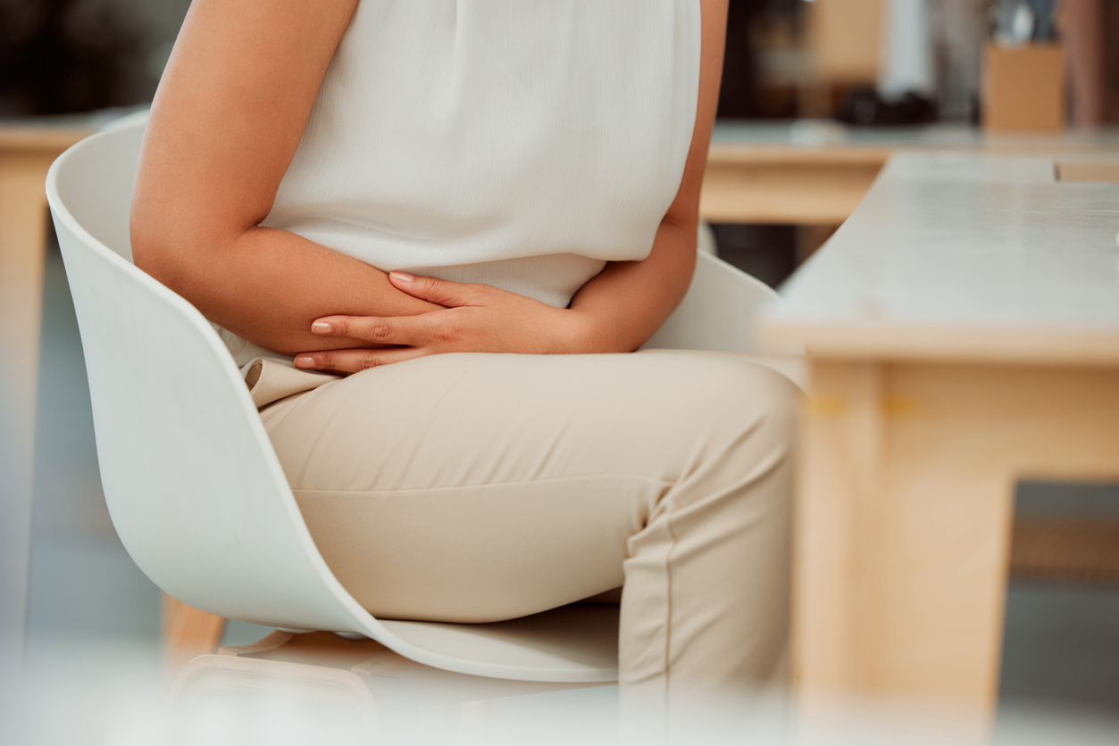 Closeup of woman holding sore abdomen. Sitting in a chair.