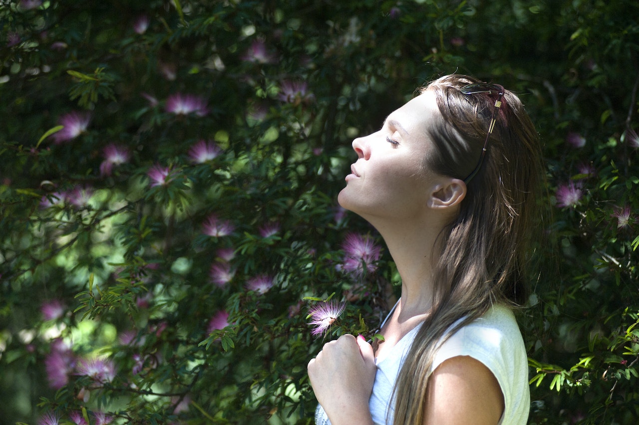 Managing asthma well allows this woman to breath deeply next to a climbing vine with yellow and white flowers.